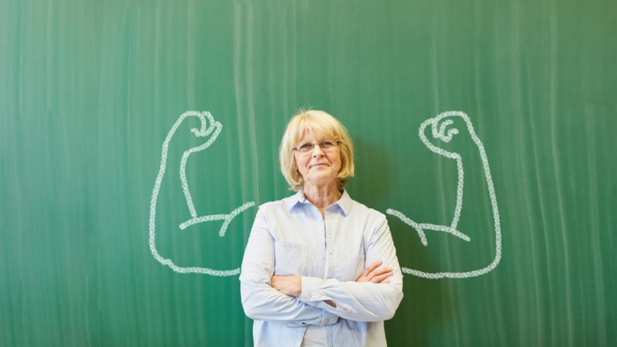 Einer Lehrerin steht vor der Tafel. Darauf sind muskulöse Arme gezeichnet.