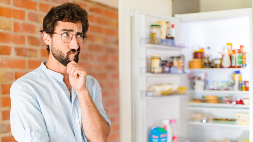 Ein Mann steht nachdenklich vor einem geöffneten Kühlschrank