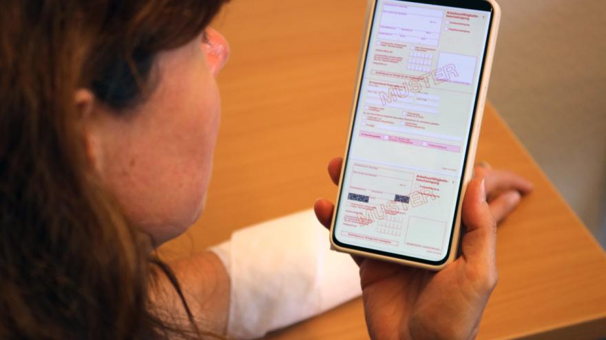 Frau hält Smartphone mit Arbeitsunfähigkeitsschein in der Hand