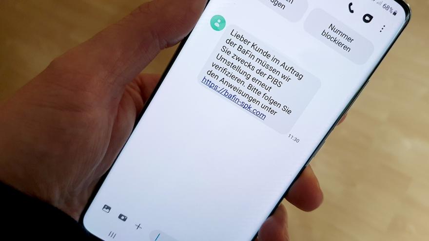 Hand hält Smartphone, Display zeigt betrügerische SMS zum Online-Banking