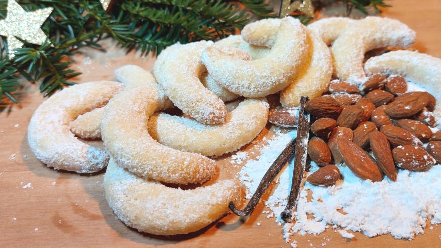 Vanillekipferl auf einem Tisch mit Mandeln und einem Häufchen Puderzucker