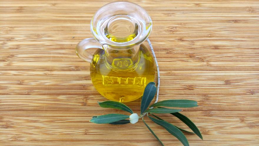 Glaskaraffe gefüllt mit Olivenöl daneben ein Olivenzweig