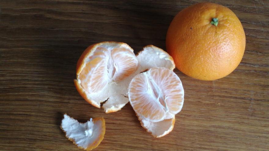 Eine zur Hälfte abgeschälte Mandarine liegt neben einer ungeschälten Mandarine auf einem Holztisch