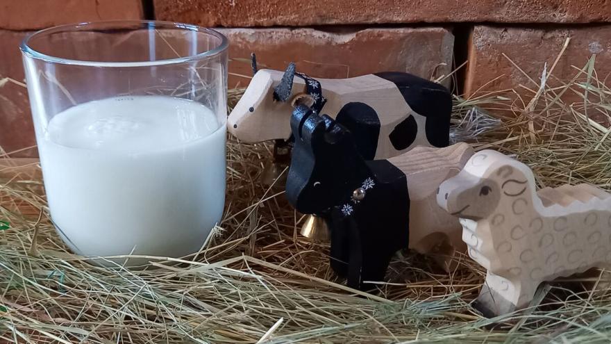 Kuh, Schaf und Ziege als Holzfiguren stehen neben einem Glas Milch.