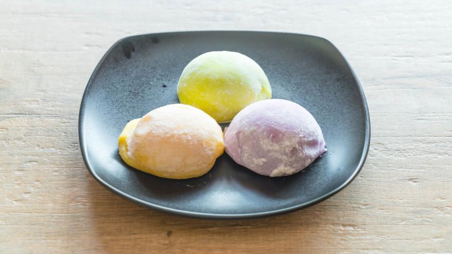 Drei Kugeln Mochi-Eis auf einem dunklen Teller.