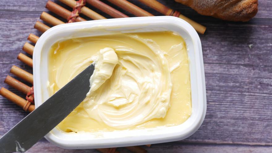 Eine offene Margarinepackung steht auf einem Tisch, ein Messer mit etwas Margarine liegt darauf.