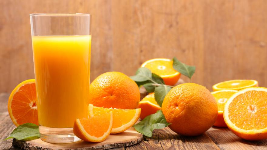 Ein Glas Orangensaft steht auf einem Tisch. Daneben liegen aufgeschnittene und ganze Orangen.
