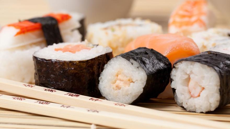 Sushirollen mit Lachs gefüllt liegen auf einer Sushimatte. Davor liegen zwei Essstäbchen.