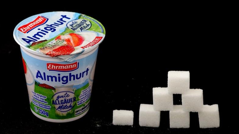 Joghurtbecher von Ehrmann Almighurt und daneben eine Zuckerwürfel-Pyramide